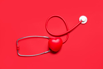 Modern stethoscope and red heart on color background