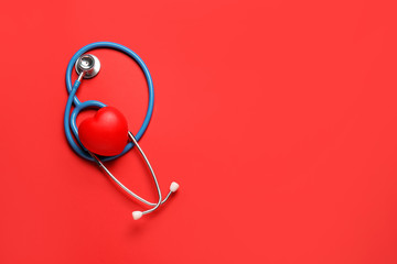 Modern stethoscope and red heart on color background