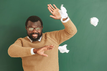 Naughty pupils throwing crumpled paper in African-American teacher near blackboard