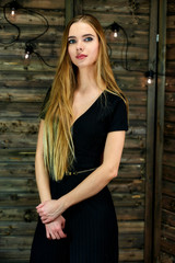Obraz na płótnie Canvas The concept of glamor, style. Vertical portrait of a pretty blonde girl with long hair and excellent make-up on a wooden background with lights. Standing in different poses in front of the camera.