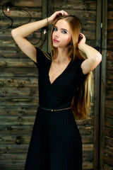 The concept of glamor, style. Vertical portrait of a pretty blonde girl with long hair and excellent make-up on a wooden background with lights. Standing in different poses in front of the camera.