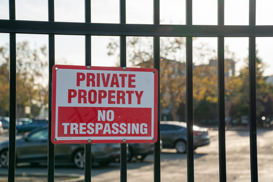 Private property no trespassing sign on black gate in front of parking lot