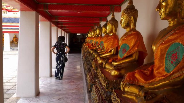 A woman walks past a row of Buddha statues at Wat Pho Temple in Bangkok.