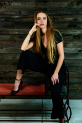 The model sits in various poses in front of the camera on a stand. The concept of fashion and style. Portrait of a pretty blonde girl with long hair and great makeup on a wooden background.