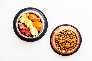 Healthy feed for cats and dogs. Bowls full of dry feed, meat and vegetables on white background top-down