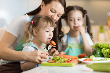 family mom with children daughters chopping vegetables in home kitchen