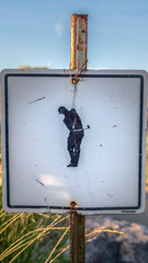 Vertical frame Focus on a weathered sign at a golf course against road and grassy land
