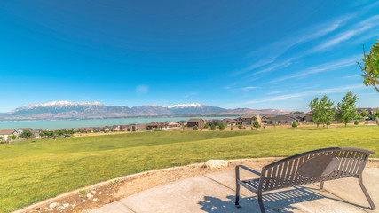 Fototapeta na wymiar Panorama frame Park metal bench with view of lake snowy timpanogos mountains and blue sky
