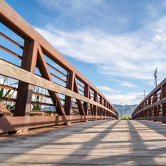 Square Focus on bridge with brown lattice metal railing and sunlit wooden deck