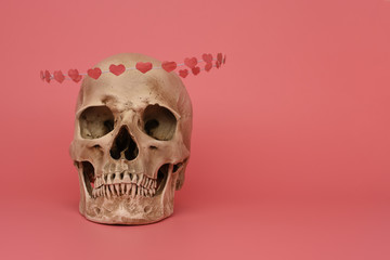 The replica of human skull with flying hoop of paper hearts isolated on a pink background. Valentine's day, love concept. Banner, poster, breaking, postcard. Copy space, place for text