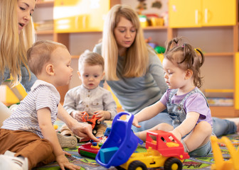 Kids toddlers playing in kindergarten or daycare centre under the supervision of moms