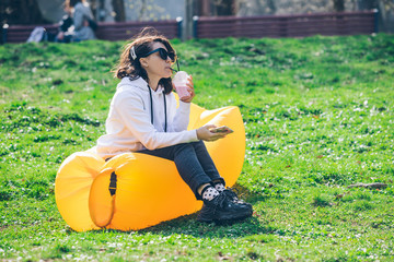 young pretty woman on yellow inflatable mattress in city park surfing in phone