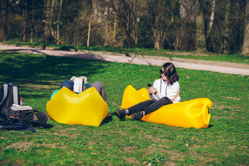 couple laying on yellow inflatable mattress in city park. reading book. taking selfie