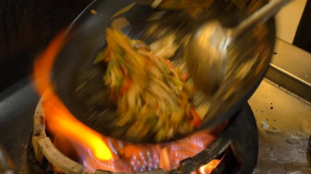 Chef Stir frying Noodles with fresh chopped colorful vegetables on a large open flame, forming a traditional Asian dish.