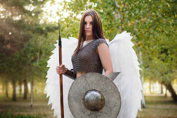 Portrait of a warrior woman in chain mail with steel bracers and wings behind her back. Standing in...