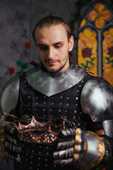 Knight in the castle with a crown in his hands. Coronation. A man in armor holds a crown.