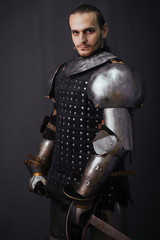 Portrait of a medieval knight with a two-handed sword. Warrior in the studio on a dark background.