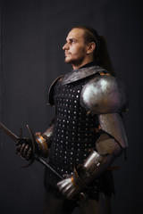 Portrait of a medieval knight with a two-handed sword. Warrior in the studio on a dark background.