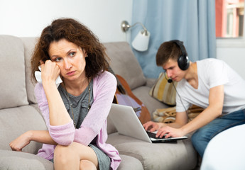 Upset woman on background with son playing on laptop