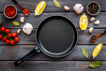 Cooking mockup. Frying pan among spices and vegetables on dark wooden desk top-down copy space - obrazy, fototapety, plakaty