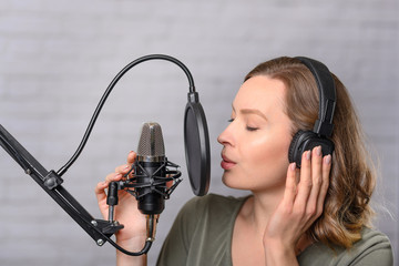 Female vocal recording. Young girl with microphone and headphones in recording studio. Recording of...