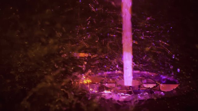 Splashes of fountain. Slow motion of water illuminated in colorful falling on fountain which change it water color in night. Wonderful multicolored fountain throws up high streams of sparkling water.