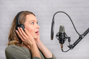 Female vocal recording. Young girl with microphone and headphones in recording studio. Recording of vocal, blogger, reading text, voice acting.