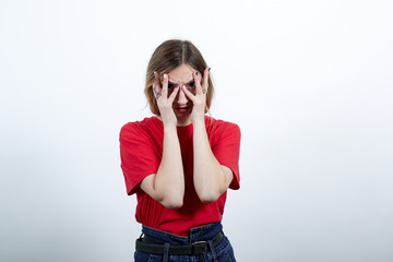 Attractive woman in red shirt having nice glasses. covered eyes with hands, looking through fingers at camera isolated on white background in studio. People sincere emotions, lifestyle concept.