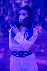 Fototapeta na wymiar Neon. Biohazard. Woman in a hazmat suit wearing a respirator with dreadlocks in the woods with smoke bombs. Concept of radiation pollution and nuclear catastrophe. Save the planet.