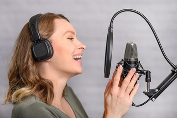 Female vocal recording. Young girl with microphone and headphones in recording studio. Recording of...