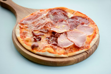 Delicious italian pizza with ham meat and parmezan cheese served on wooden cutting board, blue mint background.