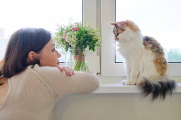 Mature woman and domestic tricolor cat sitting on the window