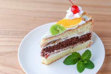 Sweet summer fruit cake with slices of orange, kiwi, cherries. frosting and whipped cream on top