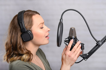 Female vocal recording. Young girl with microphone and headphones in recording studio. Recording of...