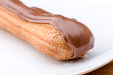 One piece of chocolate cake with vanilla cream and cherry topping served on white plate over light wooden background.
