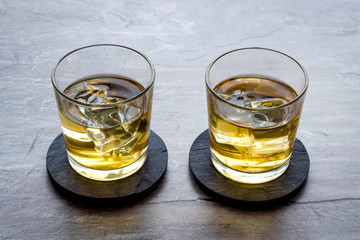 Whiskey with ice. To glasses of strong alcohol drink on grey stone background