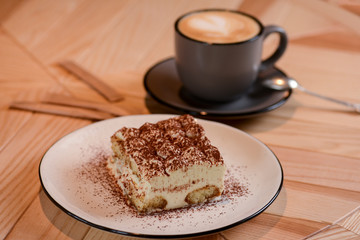 Italian stylish dessert, a piece of Tiramisu cake on a white plate and a cup of black coffee in a black cup on a table