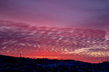 Pink dawn over a small town. City silhouette with a beautiful sunset. Dark winter landscape, outlines of mountain and forest against a background of pink, feather-like clouds. Artistically blurry.