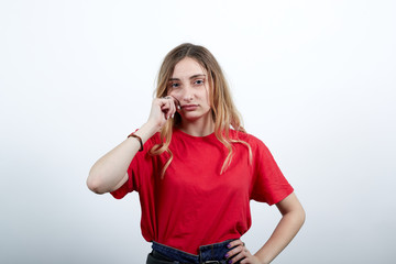 Unhappy attractive young caucasian woman in fashion red shirt pulls out cheeks, keeping hand on belt, disappointed isolated on white background in studio. People sincere emotions, lifestyle concept.