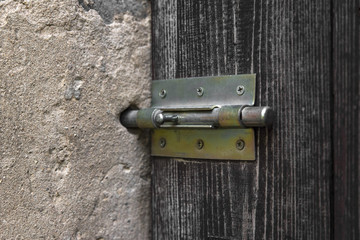 A metal bolt on a wooden door in a closed position in a concrete wall.