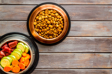 Healthy feed for cats and dogs. Bowls full of dry feed, meat and vegetables on wooden background top-down copy space
