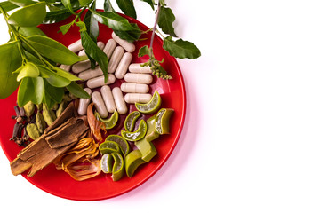 Creamy white herbal capsules, green ocimum leaves and sliced aloe vera in a dish on white background