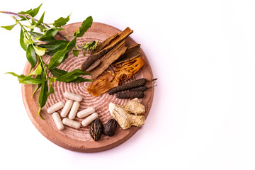Herbal medicine concept. Top view of cinnamon, dry ginger, black cardamom, mace, javitri, long pepper, and herbal capsules with tulsi leaves on a white background