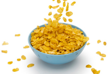 Motion blur of pouring golden cornflakes flowing into the blue bowl isolated on white background