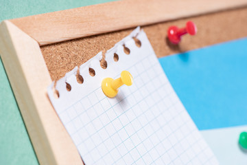 Close up of a paper sheet attached by a button on a corkboard for notes