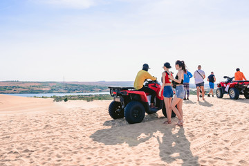 Back view of female tourists enjoy riding the quad bike or powerful fast off-road four-wheel drive ATVs at white sand dunes in Mui Ne, Vietnam.