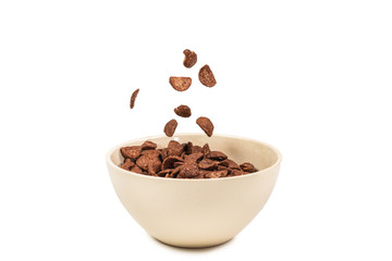Chocolate corn flakes falling to the white bowl isolated on white. Motion.