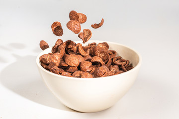 Chocolate corn flakes falling to the white bowl isolated on white. Motion.
