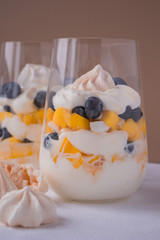 Eton mess - whipped cream, meringue, fresh blueberries and mango in glasses on a light table. Traditional English dessert. 