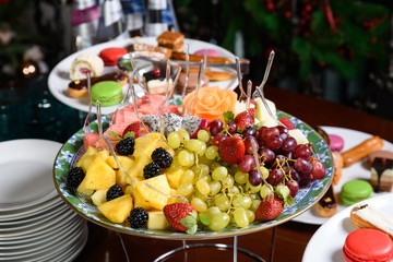 Sliced fruit on a plate with skewers and plates of sweets.